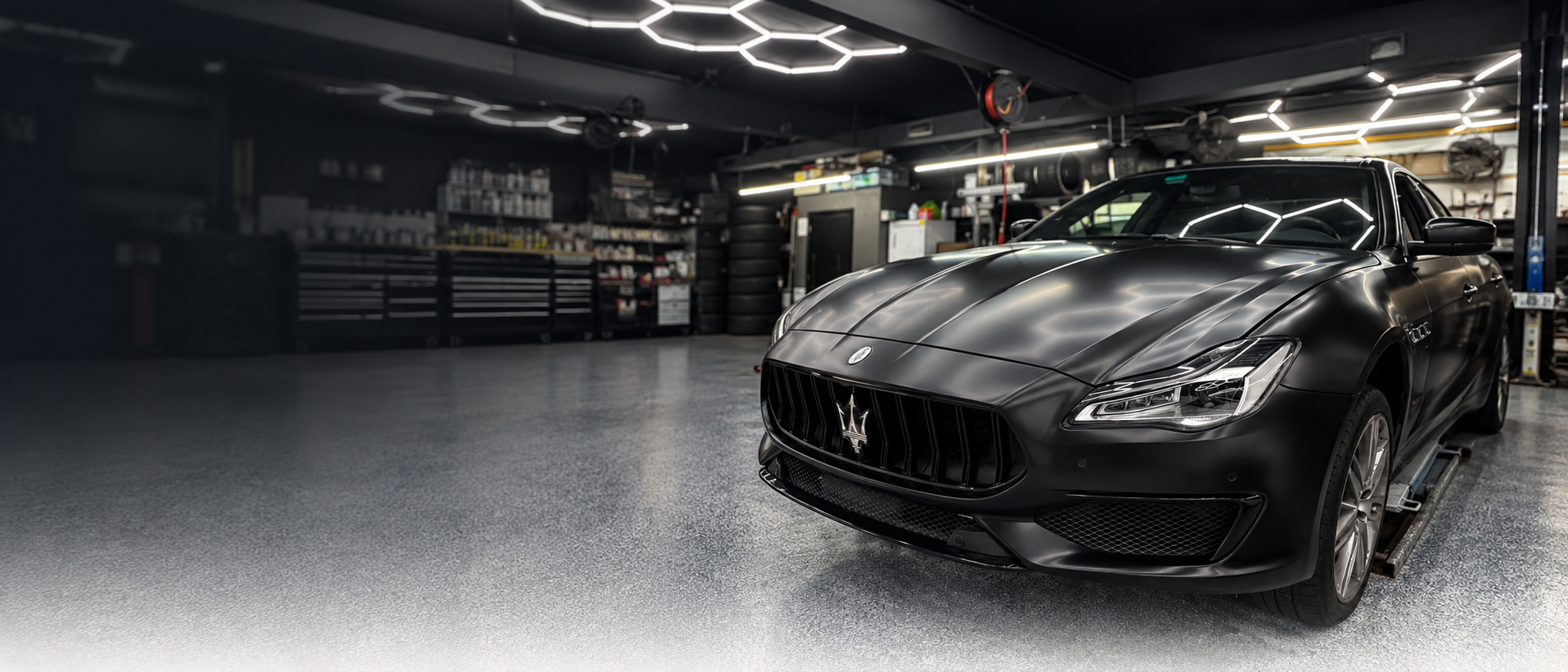 Satin black Maserati in a workshop beneath hexagonal ceiling lights